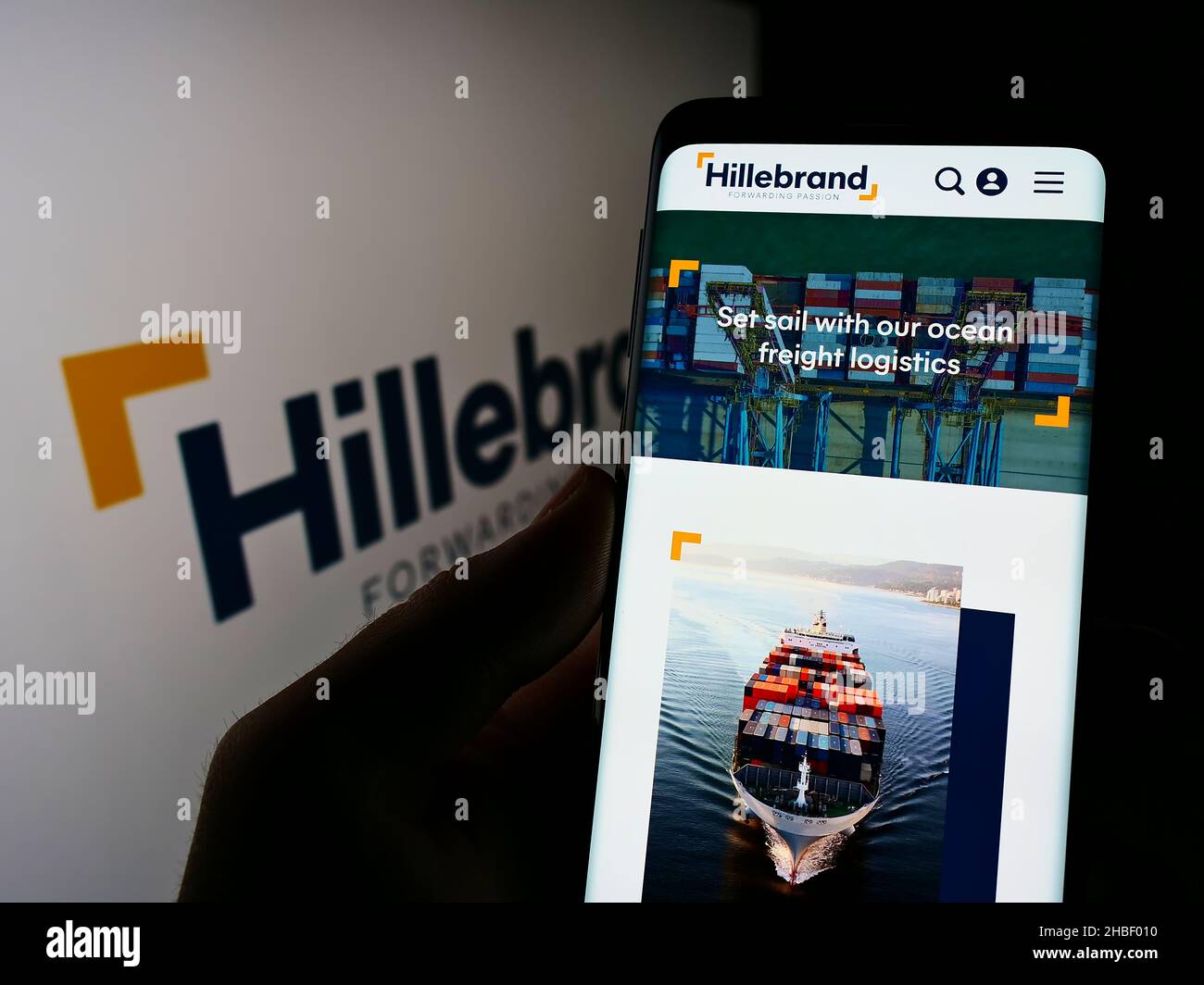 Person holding cellphone with webpage of German logistics company  J.F. Hillebrand Group AG on screen with logo. Focus on center of phone display. Stock Photo