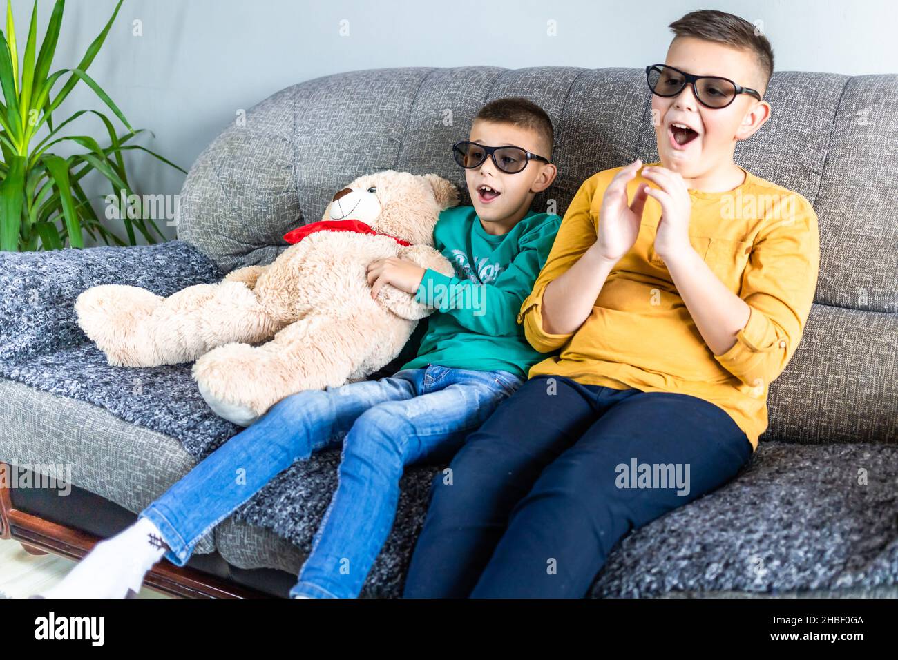 Cute boys, bothers watching movie with 3d glasses, sitting on the sofa in living room, together with teddy bear toy Stock Photo