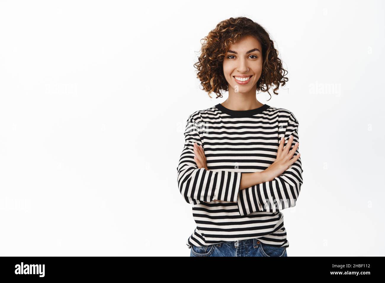Stylish modern middle eastern girl with curly short hair, posing in casual clothes against white backgrund, smiling and looking confident Stock Photo
