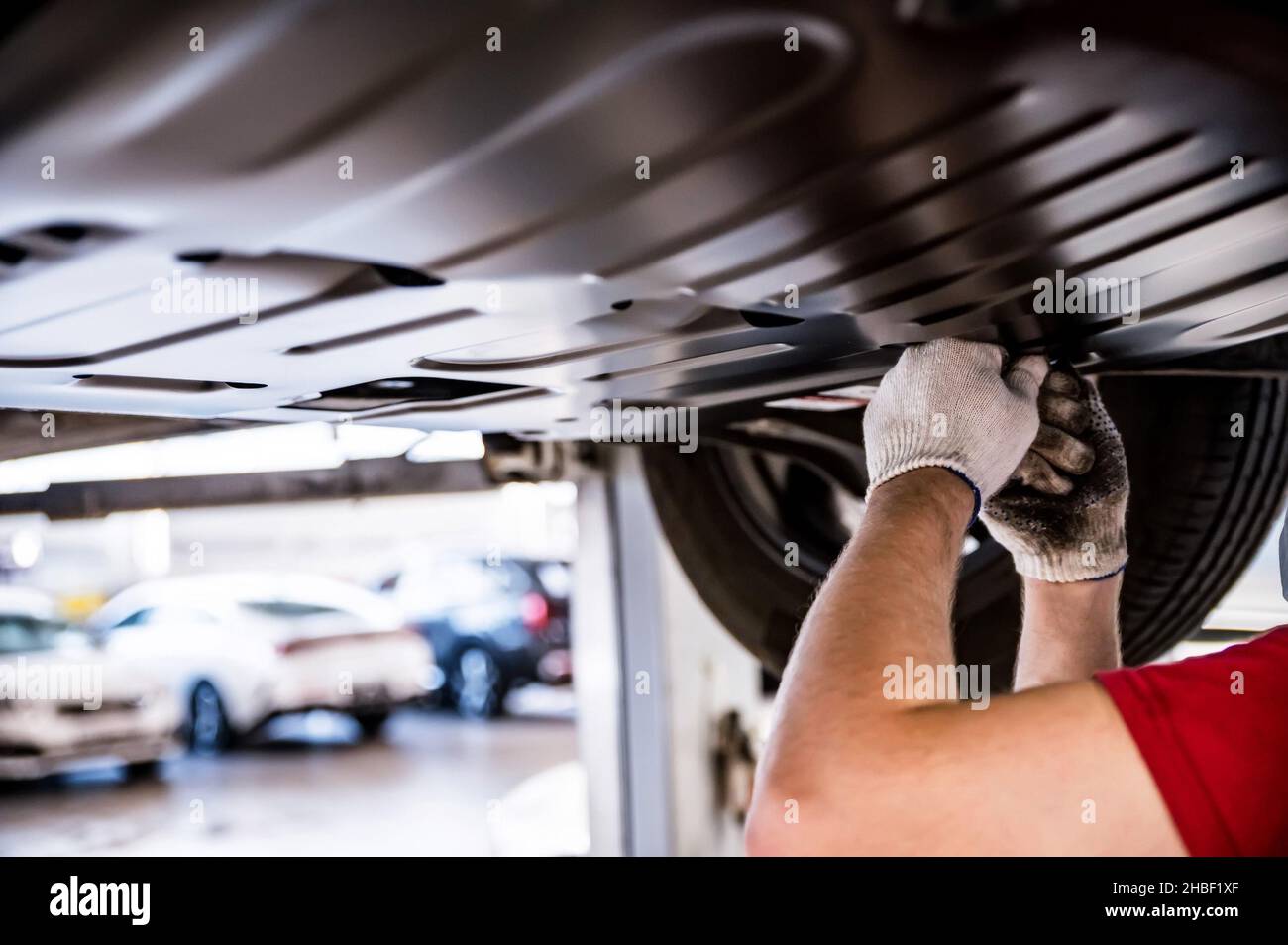 Mechanic installs underbody protection on a car raised on car lift