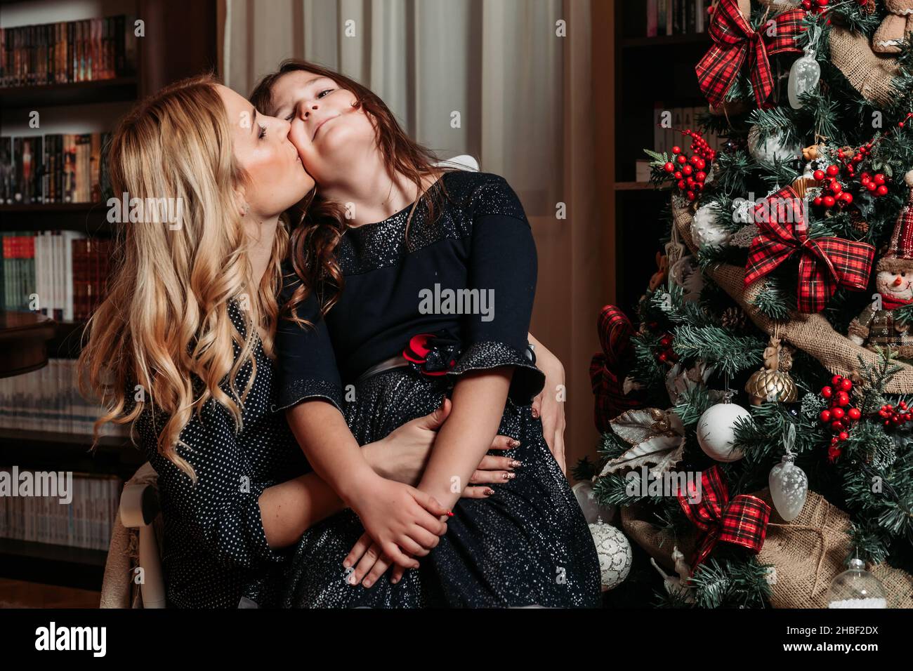 Mother and daughter sitting by the Christmas tree. Family holiday time Stock Photo