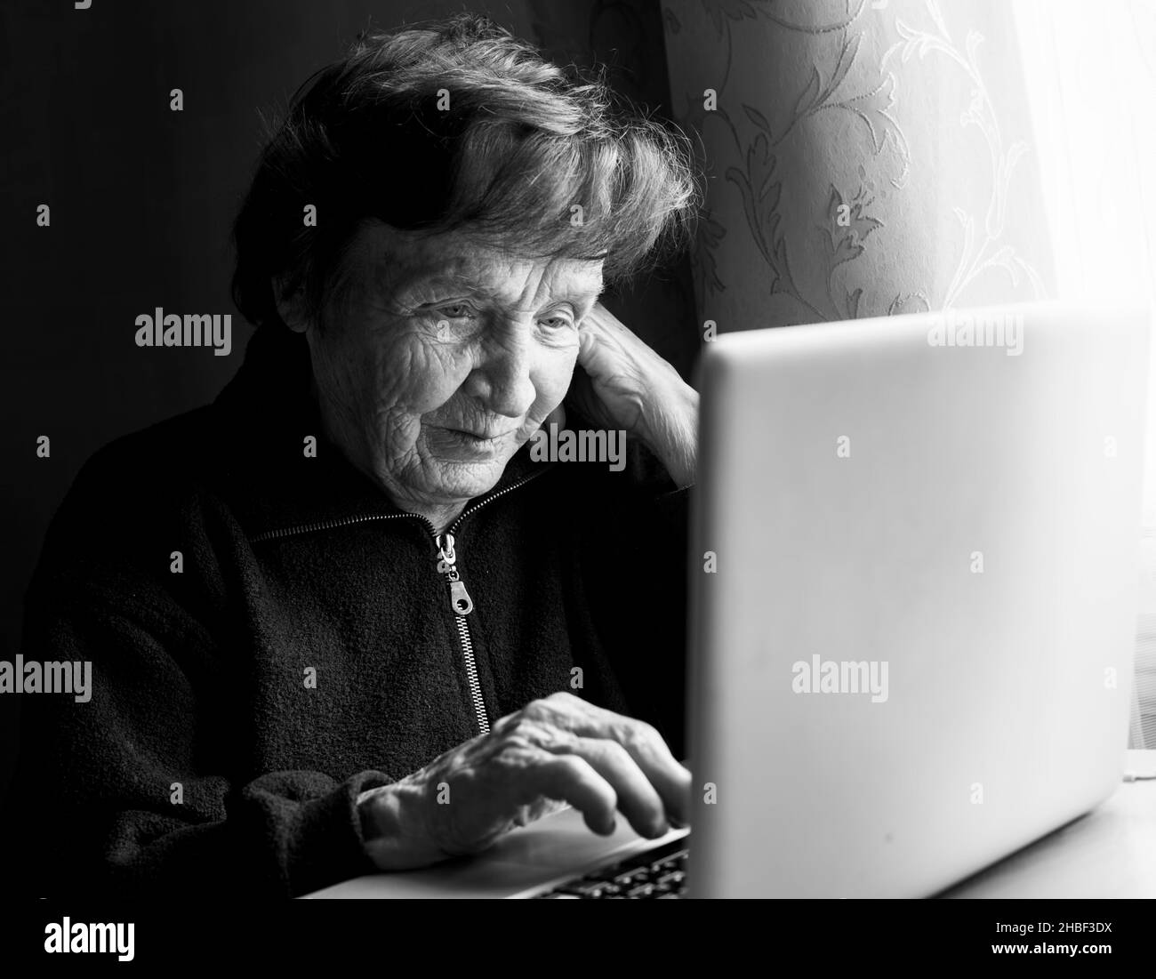 Old woman studying working on the computer in her home. Black and white photo. Stock Photo