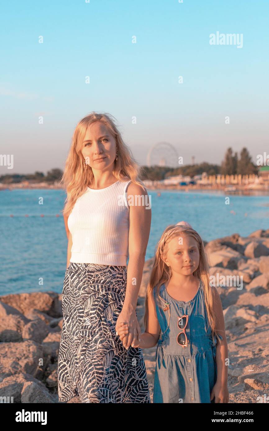 Mom with her blonde daughter on the seashore at sunset. Summer rest and entertainment. Stock Photo