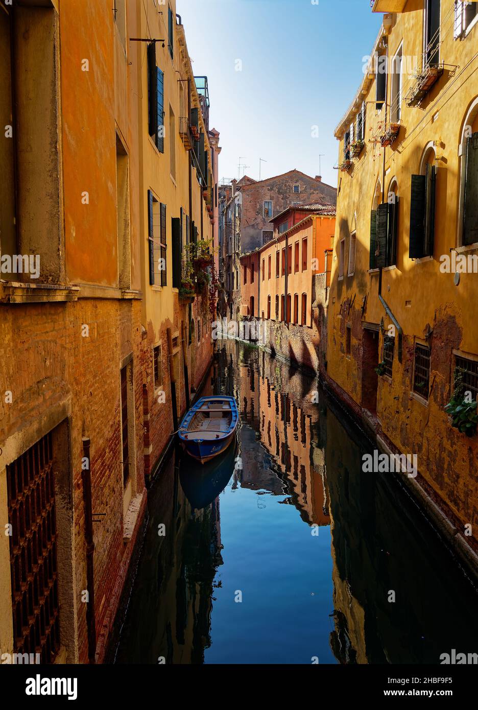 Narrow street in Venezia historical town with canal and boat, blue water and old yellow buildings in Italy. Stock Photo