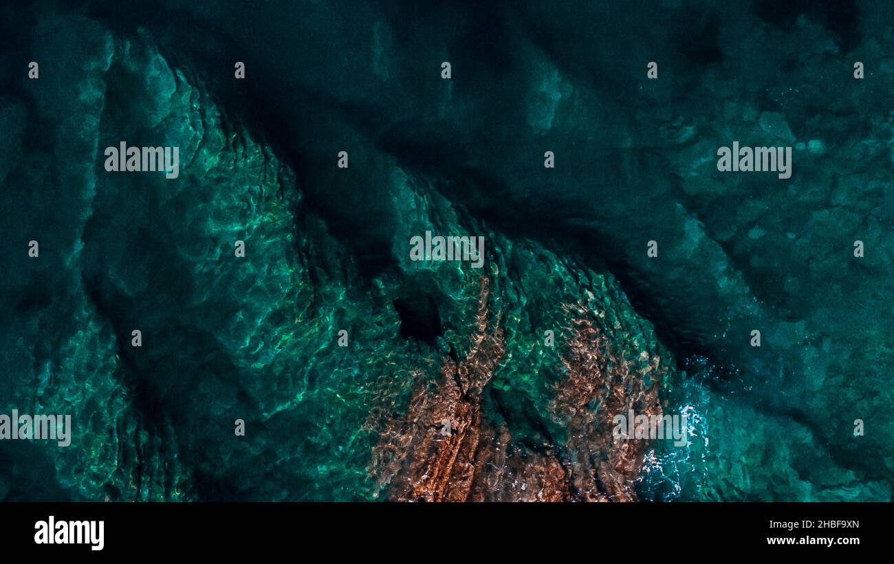 An aerial top view of green waves splashing against rocks Stock Photo ...