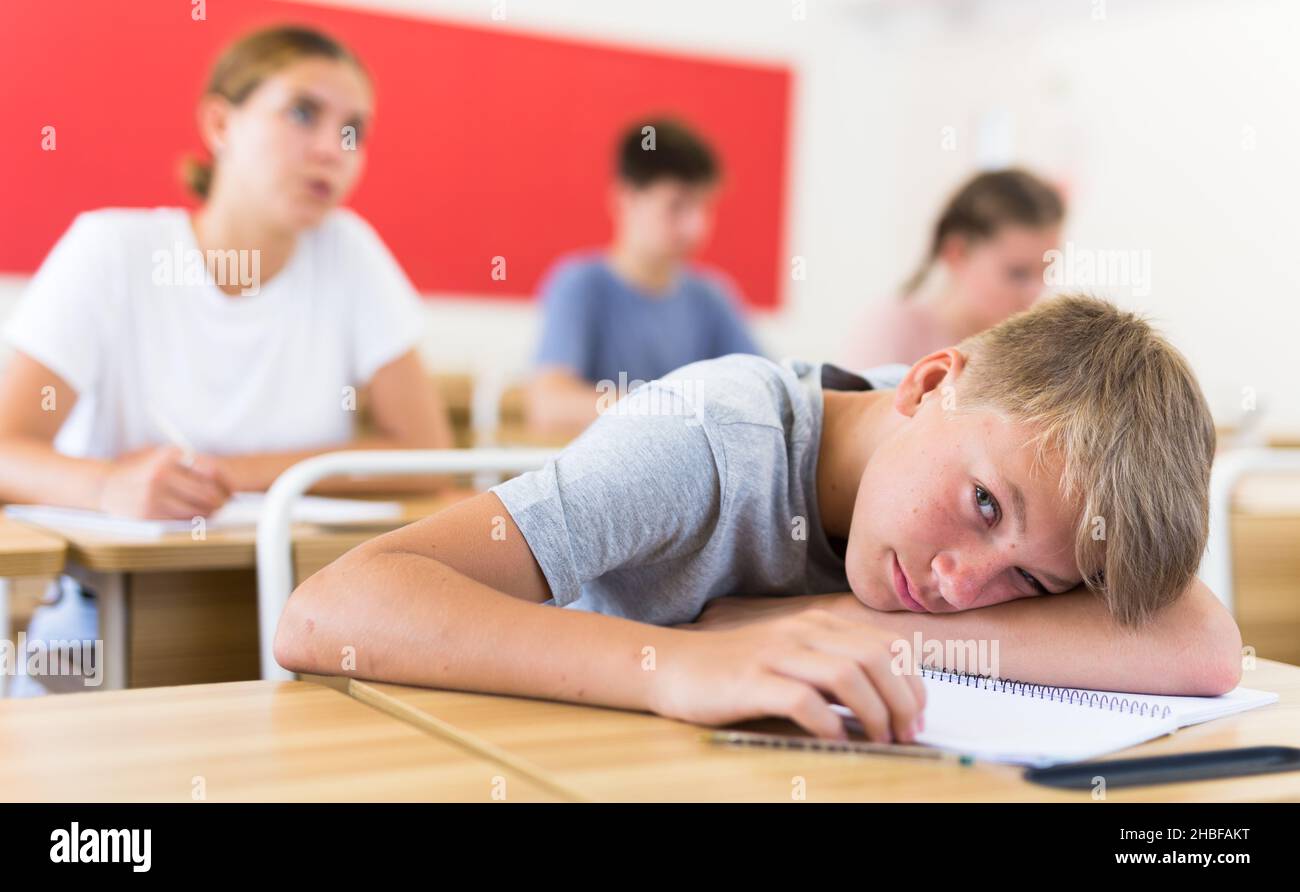 Bored teenage boy sleeping at desk in classroom during lesson Stock Photo