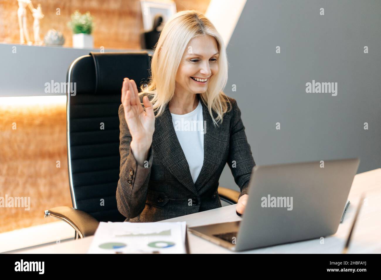 Friendly caucasian mature elegant woman top manager, ceo, sit in office using laptop, talking by