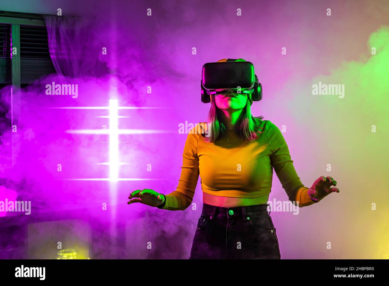Wireless technologies. Young woman using virtual reality glasses in the dark room with neon lighting. Stock Photo