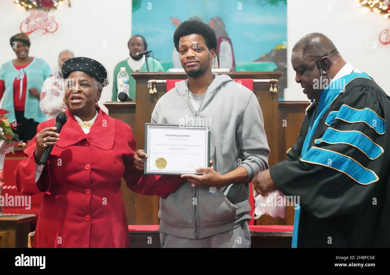 Arnez Merriweather (C) is recognized by Dr. Maggie Williams and Pastor Donald Ray McNeal for his actions of saving a baby and mother from a fire, during a service at the Hopewell Missionary Baptist Church in St. Louis on Sunday, December 19, 2021. Merrriweather saved a 3-year-old girl whose mother tossed her out of a second-floor window to escape a fire at an apartment building in north St. Louis on Monday, November 29, 2021. Merriweather then caught the mother who jumped. Merriweather, 30, said he did it by remaining calm and simply doing what was needed. Credit: UPI/Alamy Live News Stock Photo