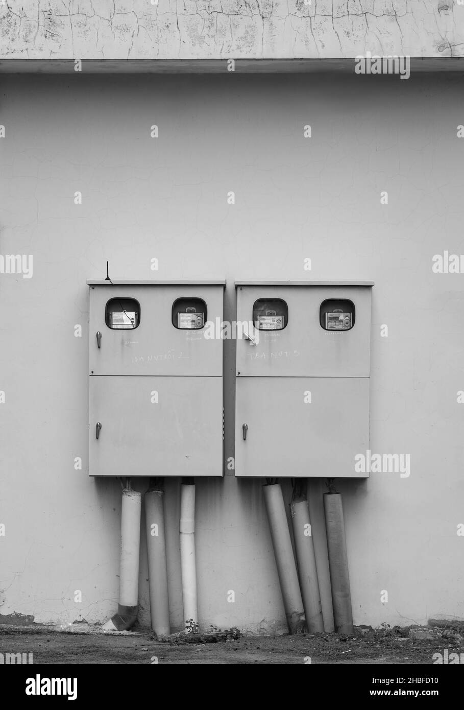 A grayscale shot of electricity boxes on the wall outside Stock Photo