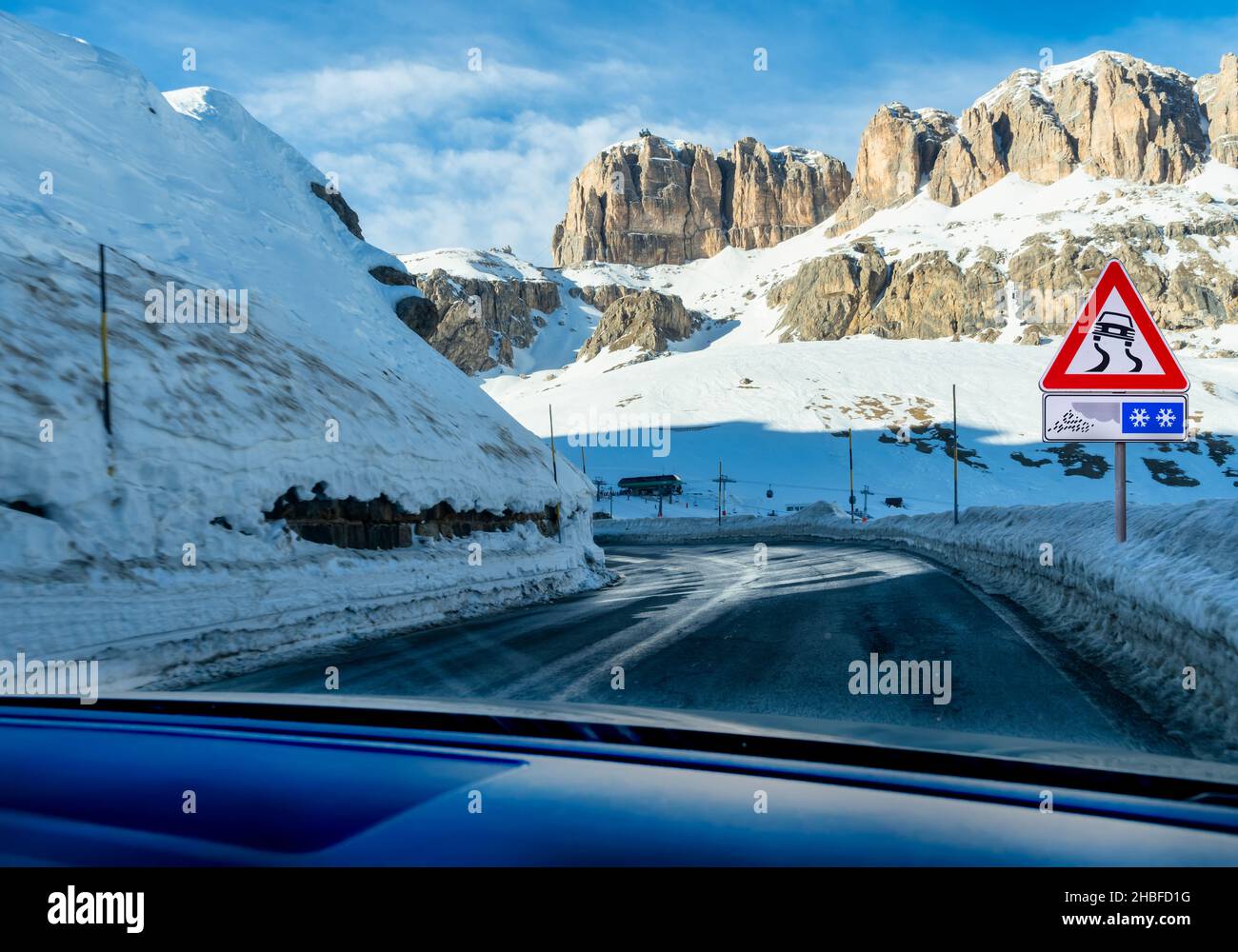 Risk of skidding in curves on a rainy or icy road in the mountains. Icy curvy road with traffic sign. Stock Photo