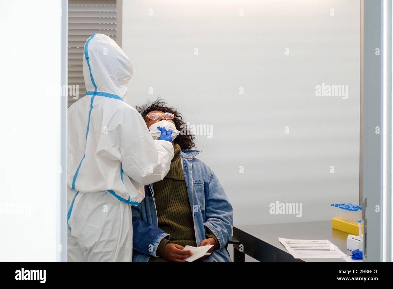 Black woman sitting to get a rapid test (SARS-CoV-2 Rapid Antigen Test) before boarding in Faro Airport, Portugal, by a nurse in protective PPE suit Stock Photo