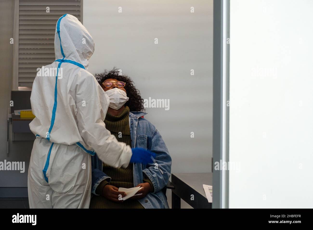 Black woman sitting to get a rapid test (SARS-CoV-2 Rapid Antigen Test) before boarding in Faro Airport, Portugal, by a nurse in protective PPE suit Stock Photo
