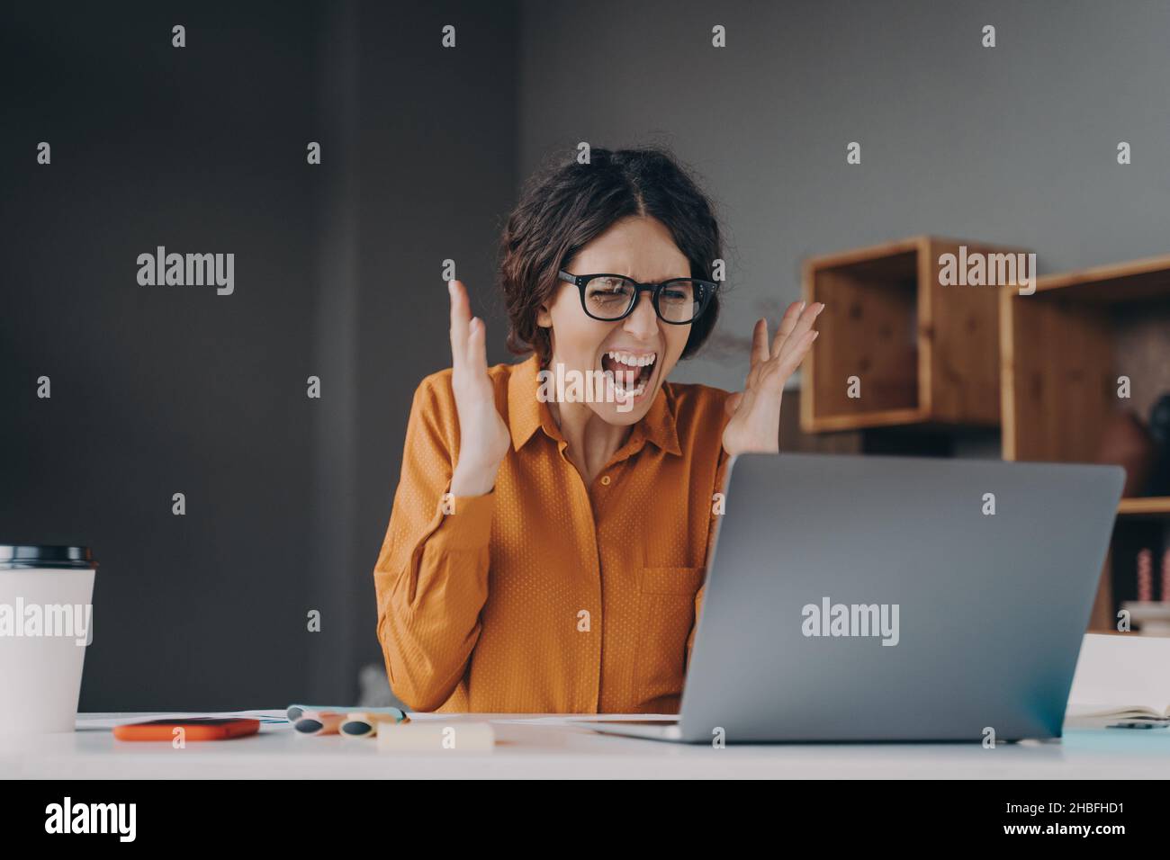 Mad Italian businesswoman shouting in distress from hopelessness while working online on laptop Stock Photo