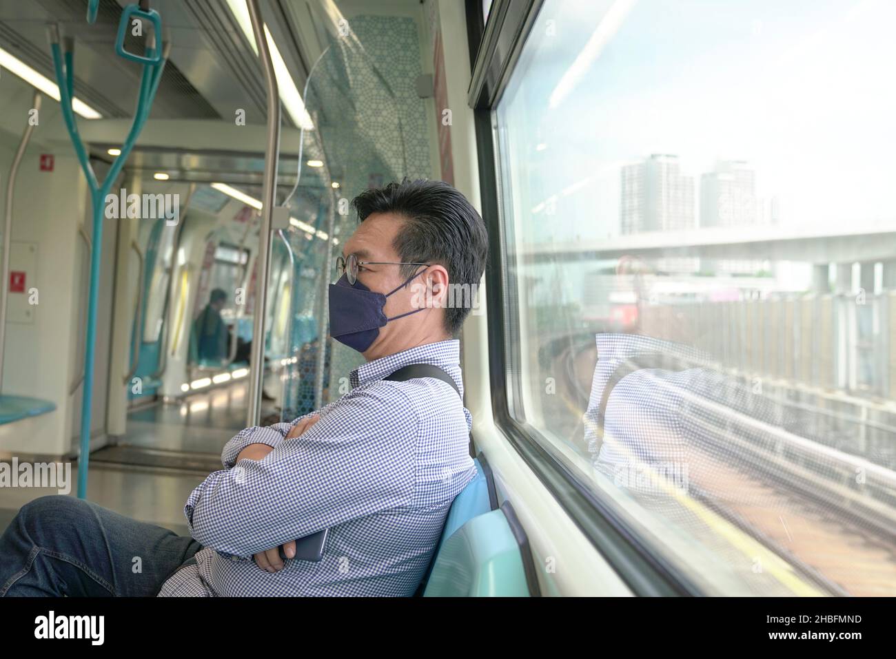Asian man commuter with face mask on inside a moving subway train. Masked transit concept Stock