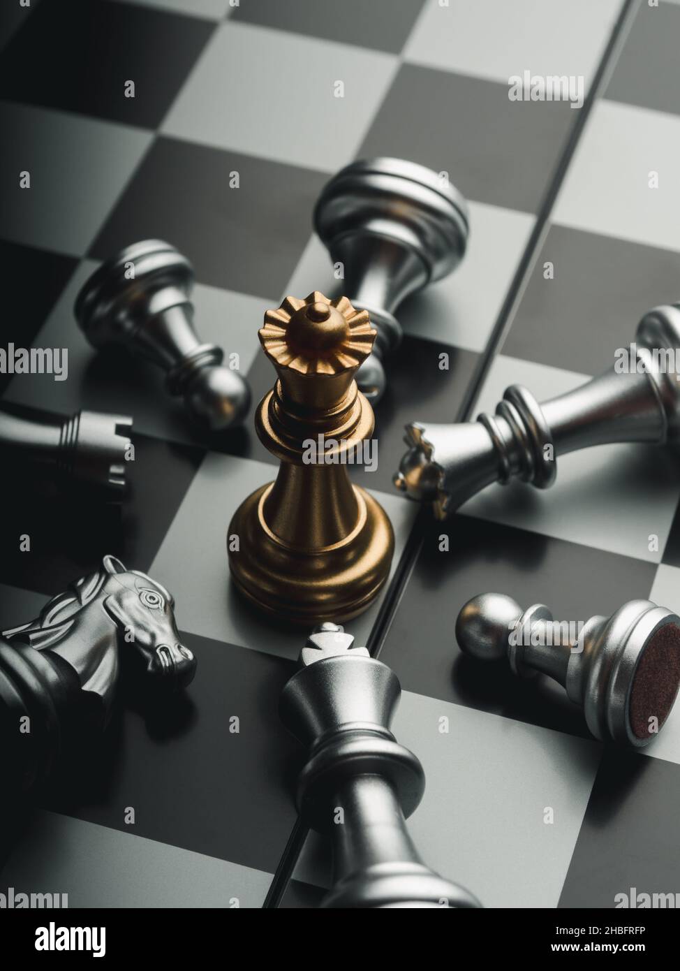 The golden queen chess piece standing with falling silver knight, rook, bishop, pawn pieces on chessboard on dark background, top view. Leadership, wi Stock Photo