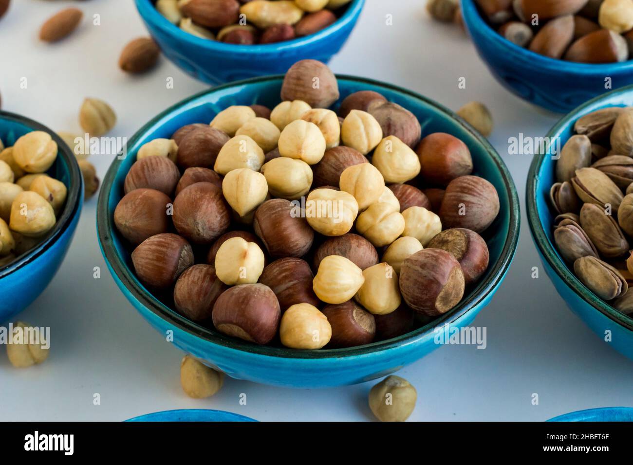 Shelled and unshelled luxury hazelnuts in a blue ceramic bowl on white surface Stock Photo