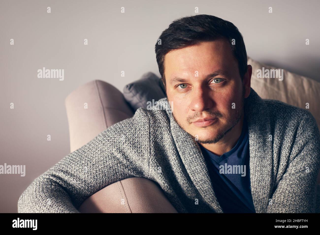 A portrait of man in a cardigan on a pink couch looks into the camera. Front view portrait.  Stock Photo