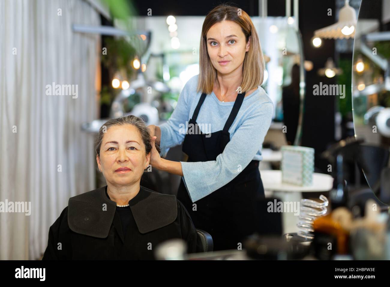 Elderly woman choosing new hairdo with hair stylist in salon Stock