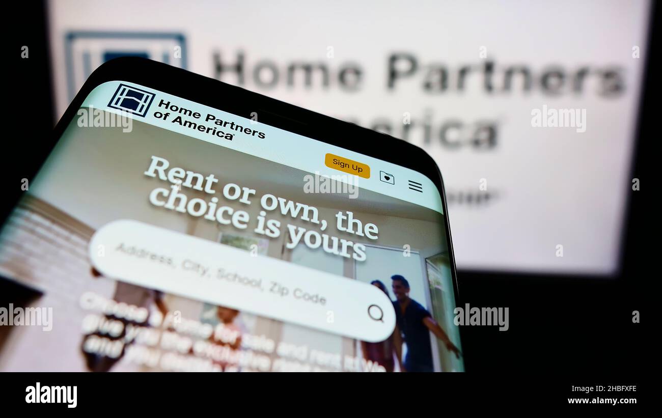 Smartphone with website of American real estate company Home Partners Holdings LLC on screen in front of logo. Focus on top-left of phone display. Stock Photo