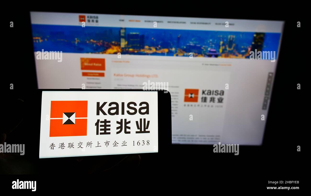Person holding smartphone with logo of Chinese property company Kaisa Group Holdings Ltd. on screen in front of website. Focus on phone display. Stock Photo