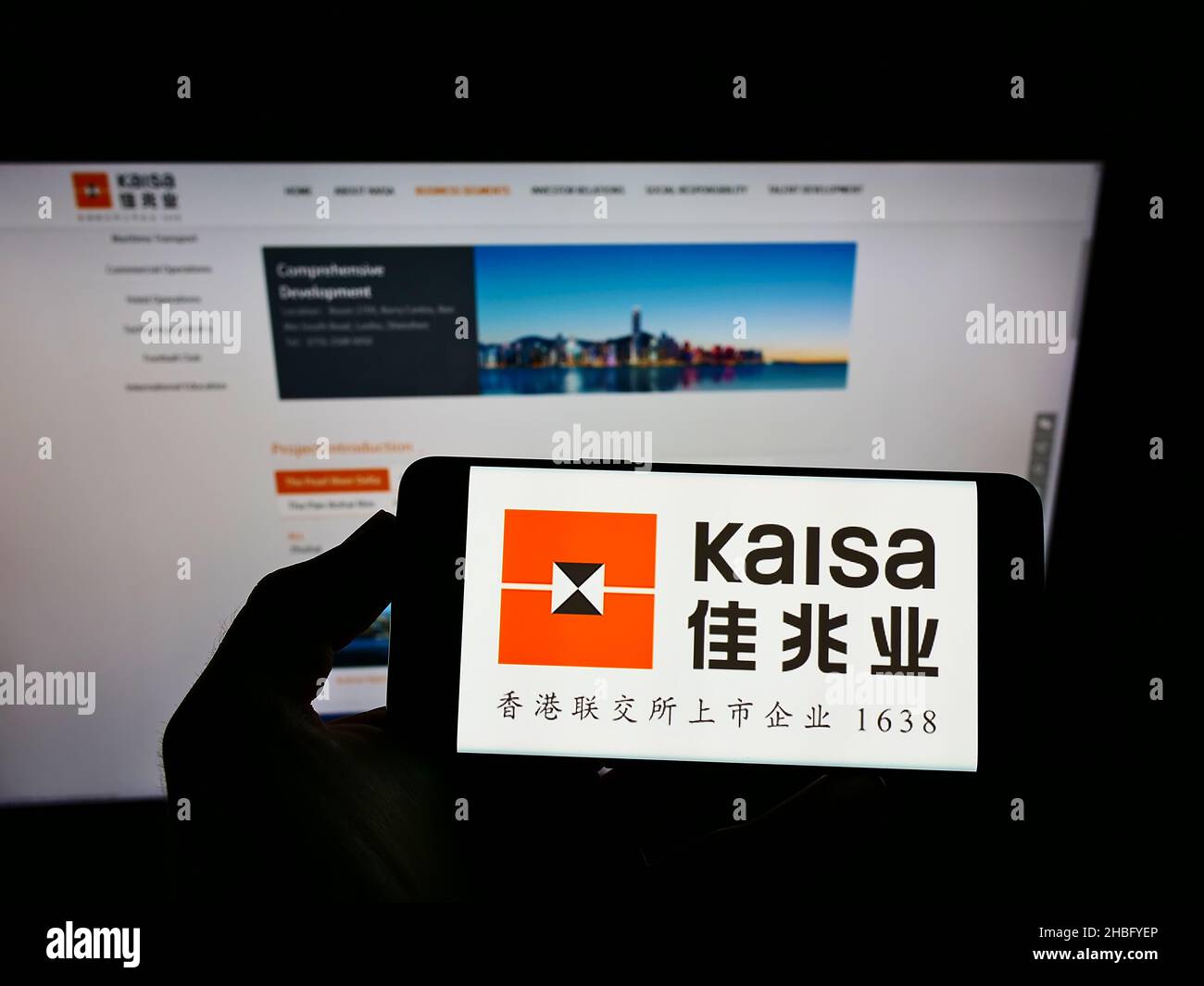 Person holding cellphone with logo of Chinese property company Kaisa Group Holdings Ltd. on screen in front of webpage. Focus on phone display. Stock Photo