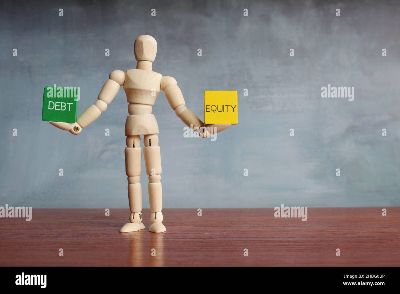 Debt and equity balance concept. Wooden human figure balancing wooden cubes with text DEBT and EQUITY. Stock Photo