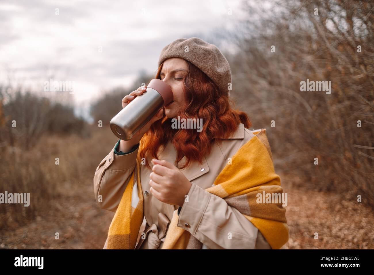 Thermos with hot drink. Happy curly hair woman drinking travel mug or steel thermo bottle. Zero waste eco concept Stock Photo