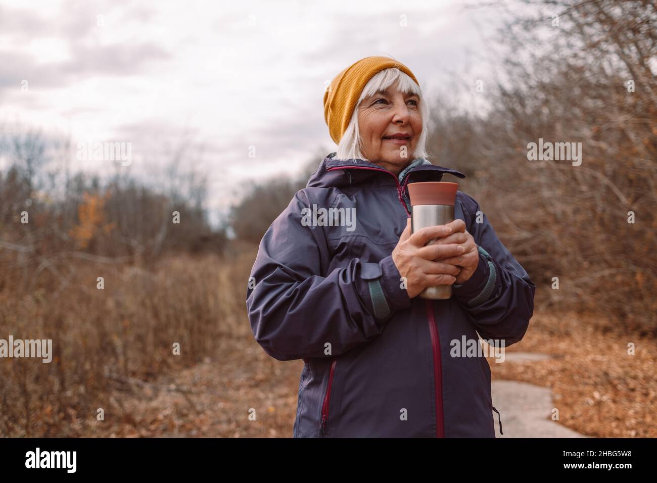 Middle age beautiful female traveler holding thermos mug in the city autumn park. Zero waste eco concept Stock Photo