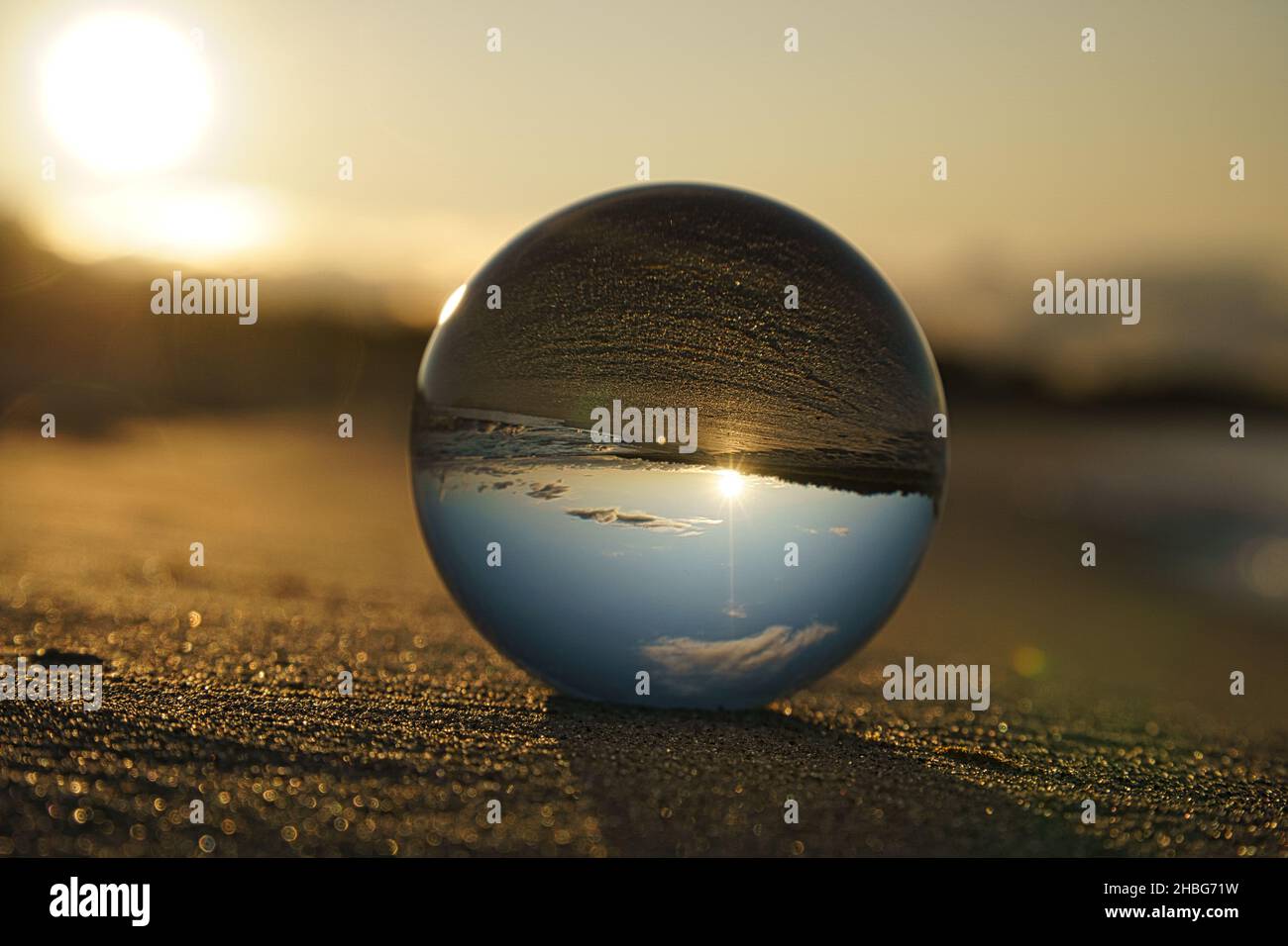 Glass globe on the beach of the Baltic Sea in Zingst in which the landscape is depicted. The sunset provides a warm light mood Stock Photo