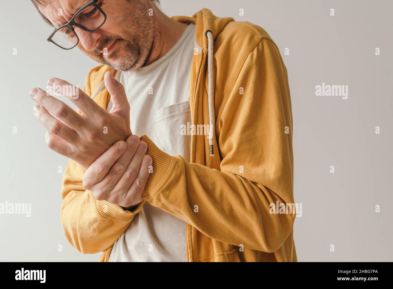 Aching wrist pain as symptom of tendonitis or arthritis, adult caucasian male with painful grimace looking down at his joint Stock Photo