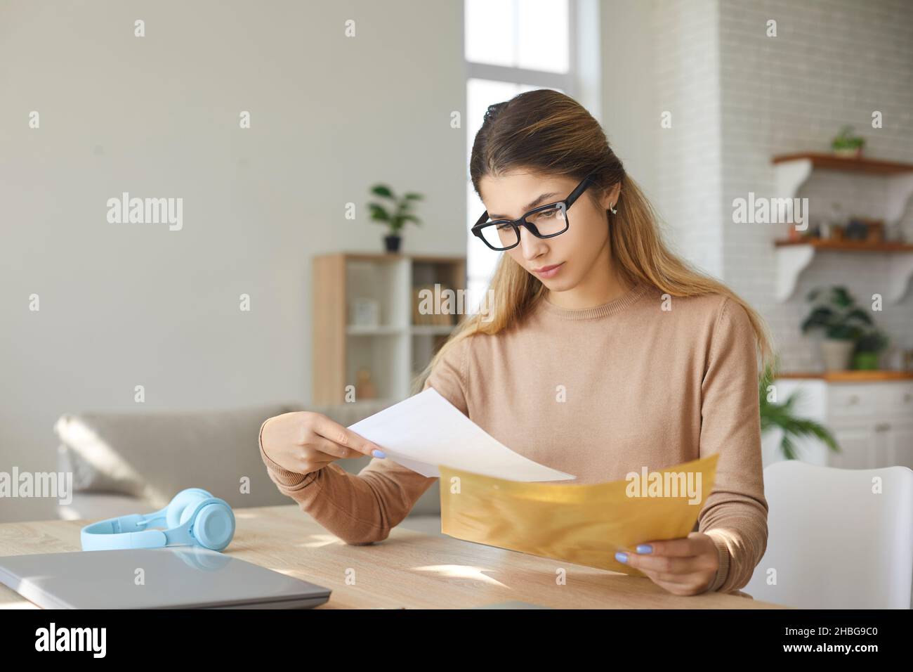Anxious young woman at home taking letter from envelope reads bad negative news. Stock Photo