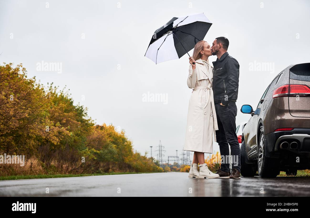 Young couple in love kissing under umbrella, standing on the road near