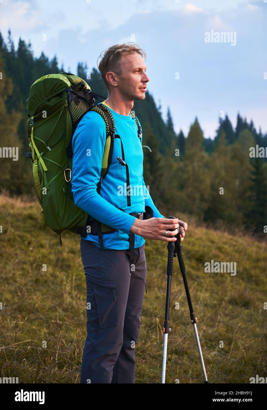 Side view of hiker male with backpack and trekking pole standing on