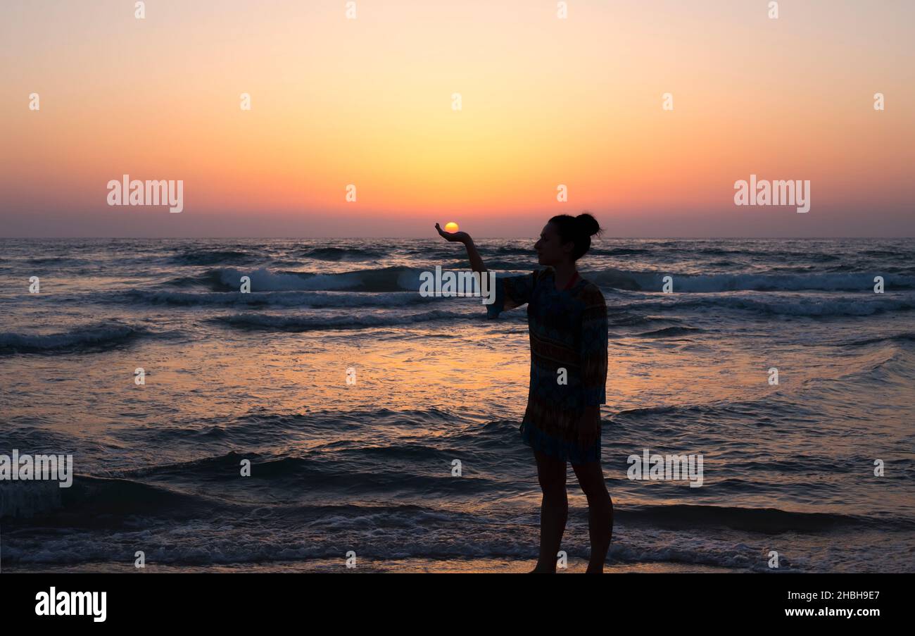 woman holds the sun as it sets in the palm of her hand Stock Photo