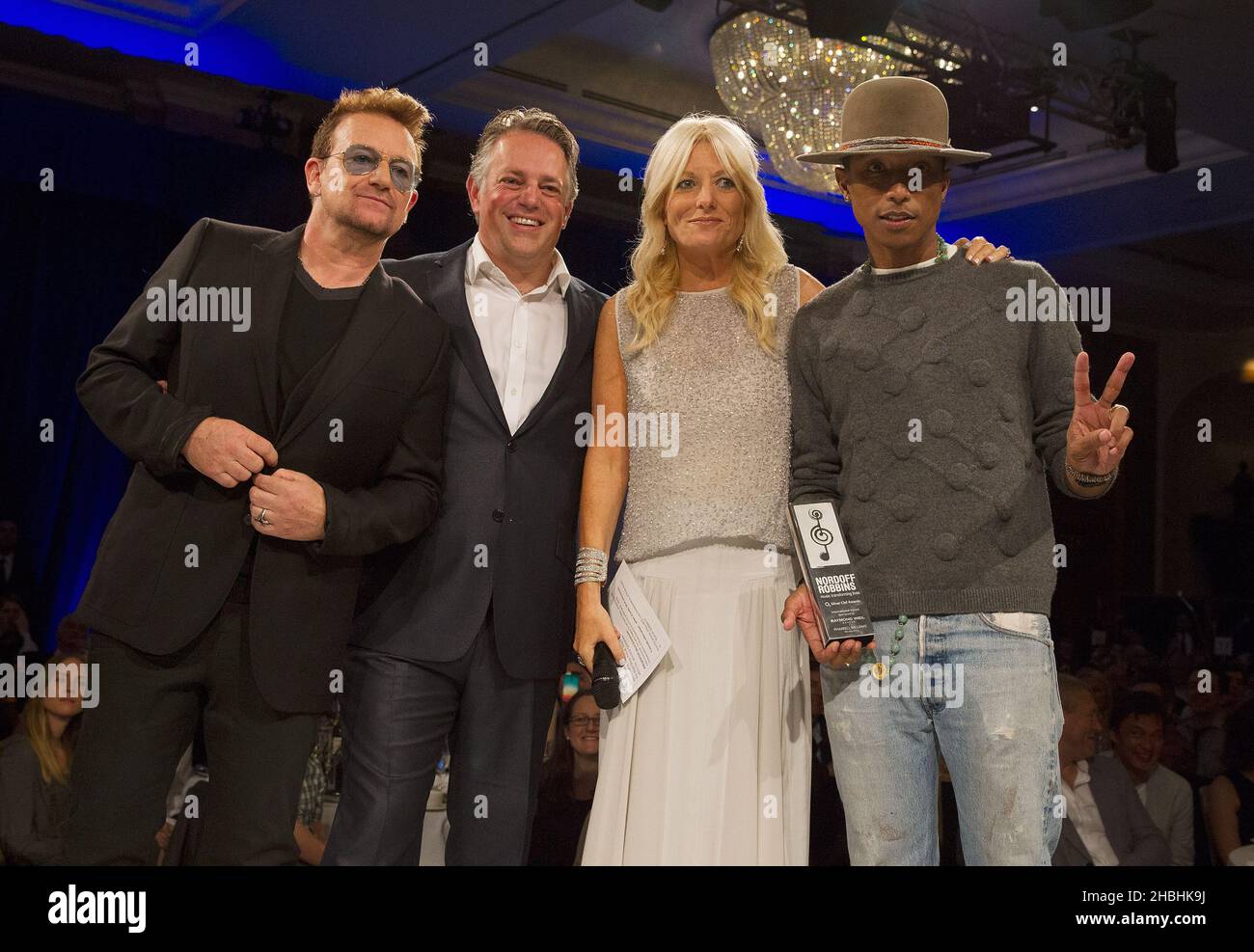 Bono (left) after presenting the Raymond Weil International Award to Pharrell Williams (far right), on stage with Gaby Roslin, at the Nordoff Robbins 02 Silver Clef Awards at the London Hilton Park Lane Hotel in London. Stock Photo