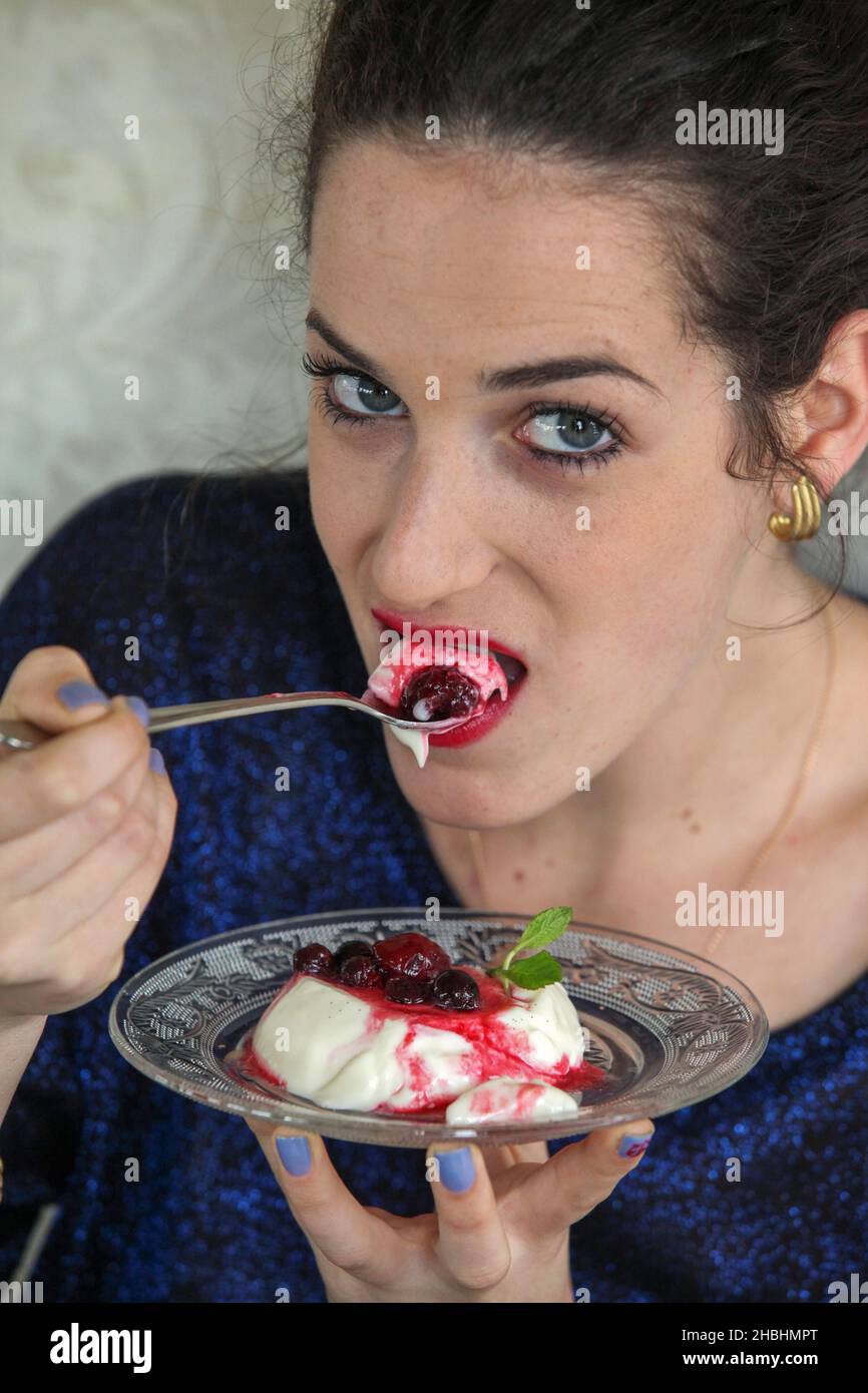 Young woman eats Panna Cotta dessert with cherries Stock Photo