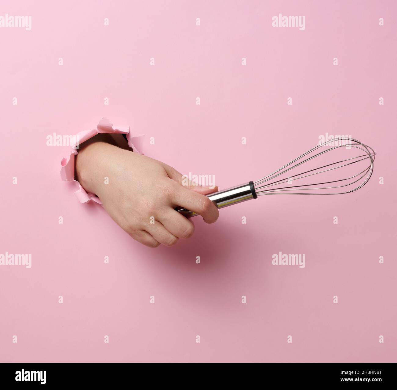 female hand holds a metal whisk for beating products on a pink