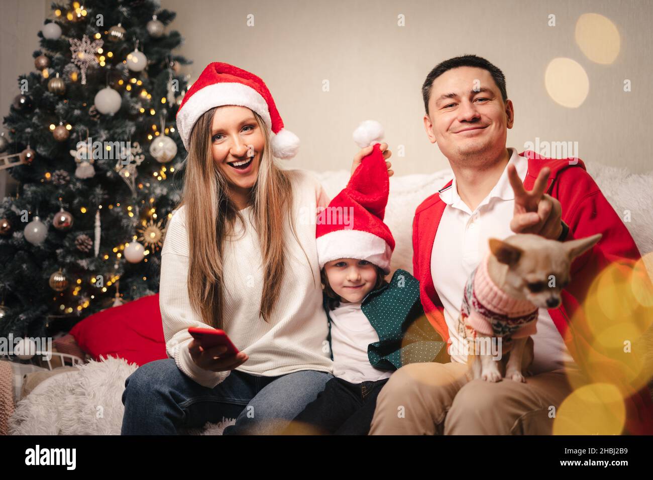 Portrait of happy family with kid son and puppy. Mother in Santa hat, father, child boy and dog in sweater having fun on Christmas holidays at home Stock Photo
