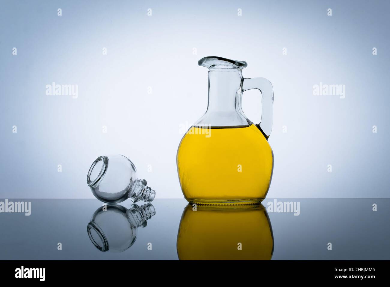 Olive oil bottle, vegetable salad flavoring. Gray background. Yellow cooking oil in a glass jar Stock Photo