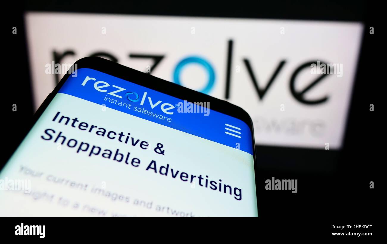 Smartphone with webpage of British mobile commerce company Rezolve Limited on screen in front of business logo. Focus on top-left of phone display. Stock Photo