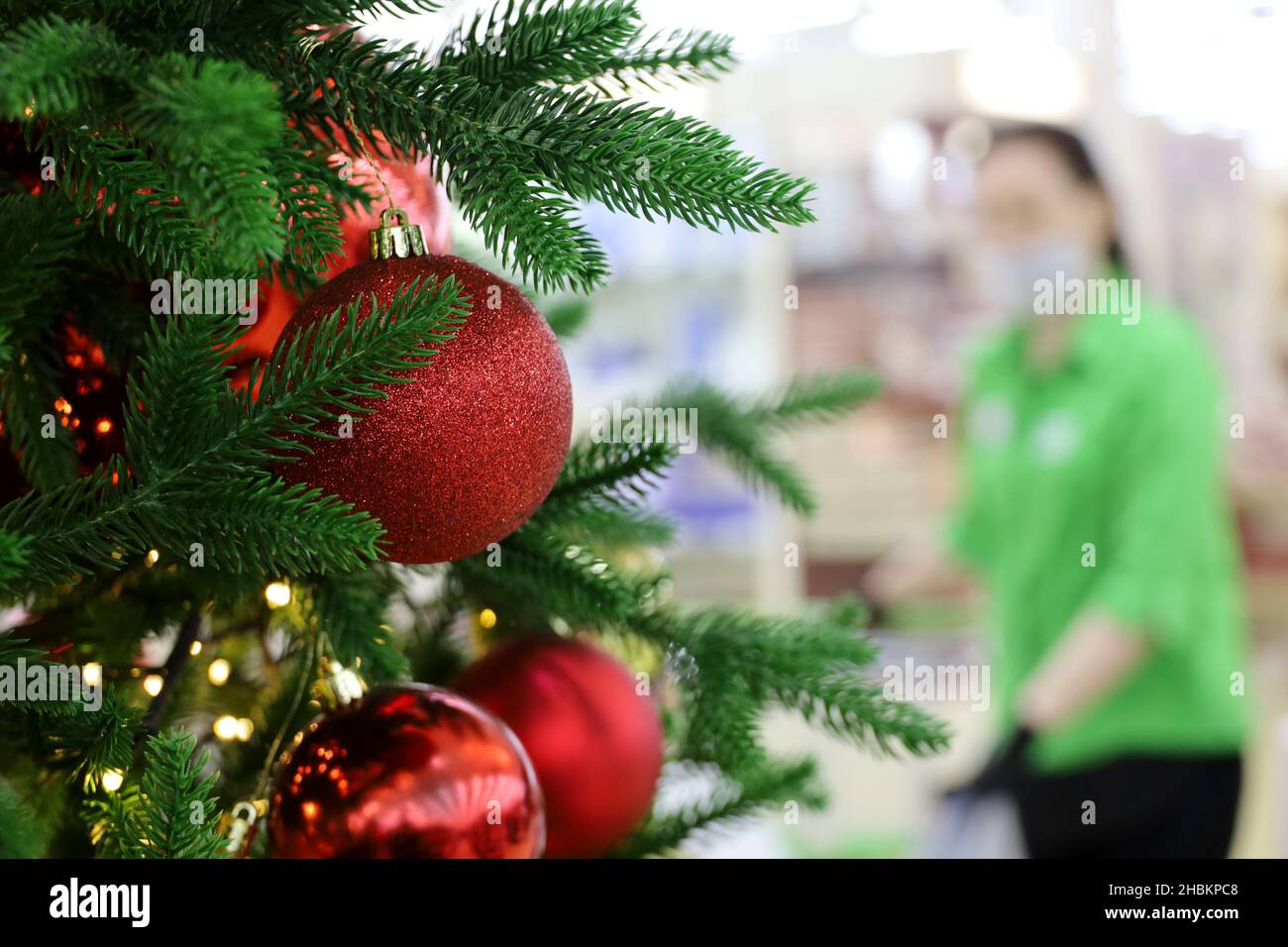 Christmas sale, New Year tree with red toy balls in a shopping mall on woman in mask background. Winter holidays, safety shopping during coronavirus Stock Photo