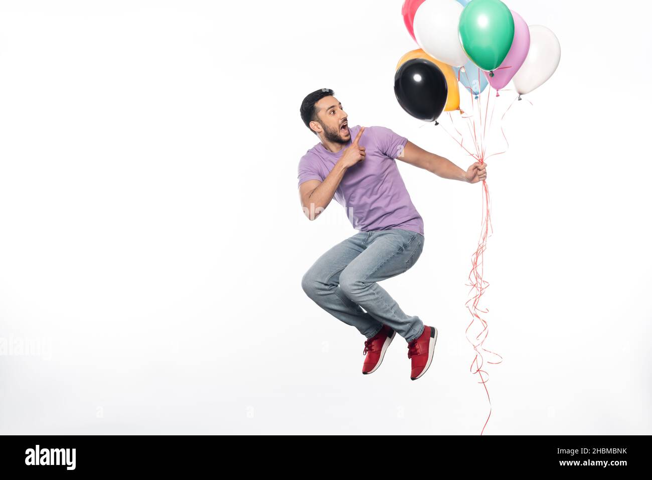 happy man jumping and pointing at colorful balloons on white Stock Photo