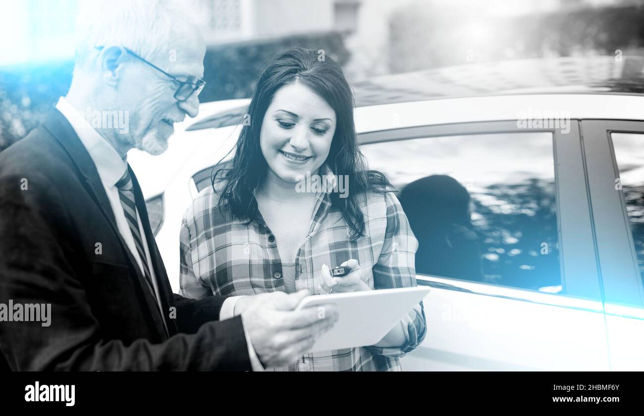 Car salesman giving explanations on tablet to pretty young woman; multiple exposure Stock Photo
