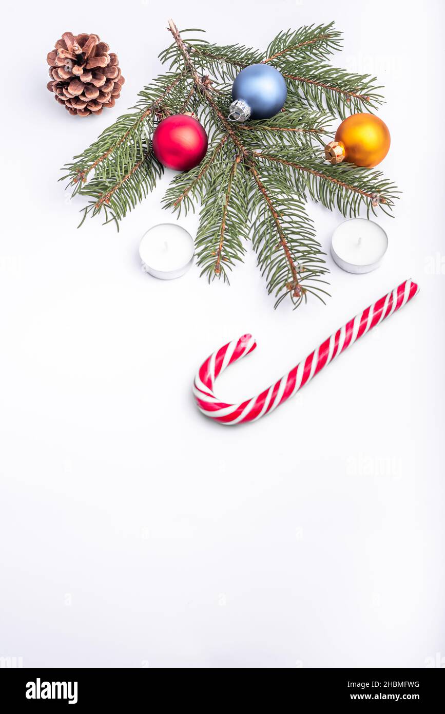 Christmas and new year flat lay: green fir branch, cone, red, blue and yellow balls, two candles and caramel candy on white isolated background. Stock Photo