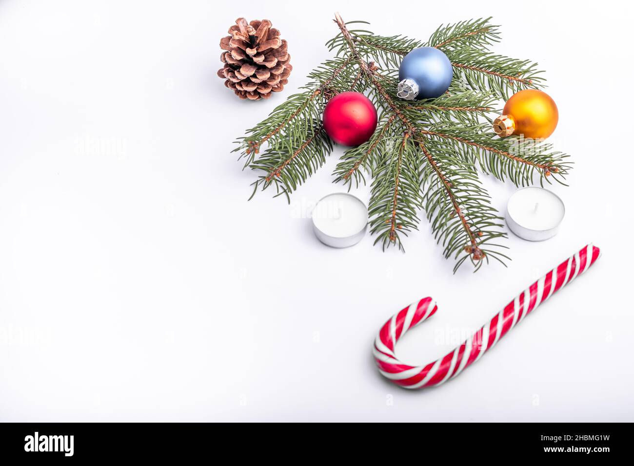 Christmas and new year flat lay: green fir branch, cone, red, blue and yellow balls, two candles and caramel candy on white isolated background. Stock Photo