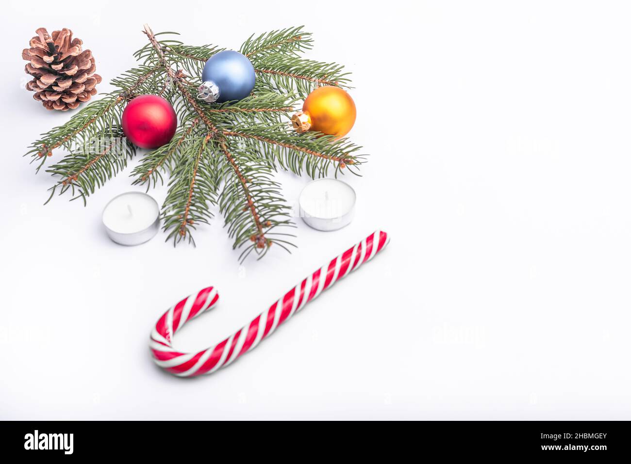 Christmas and new year flat lay: green fir branch, cone, red, blue and yellow balls, two candles and caramel candy on white isolated background. Stock Photo