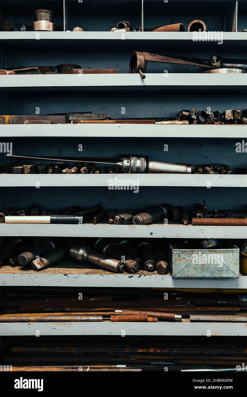 Rack with shelves in lathe shop in factory. On shelves are parts and blanks for working with metal. Industrial background. Length working place of turner. Stock Photo