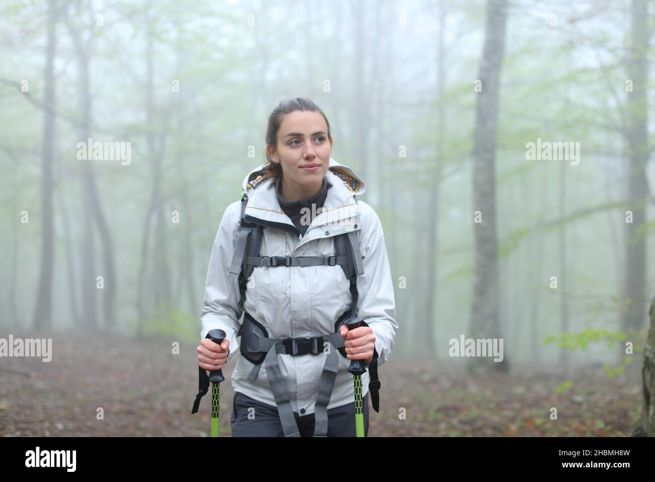 Front view portrait of a happy trekker woman walking in a forest in winter Stock Photo