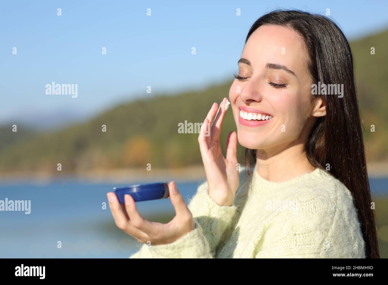 Happy woman in winter moisturizing her cheek in the mountain Stock Photo